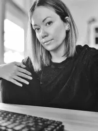 A profile picture of Daniela. She is wearing a black long sleeve, her hair is curled and rests on her right shoulder, she is smiling and looking at the camera